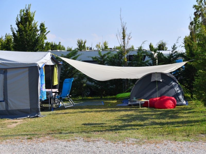 Campeggio con tenda, sedie e ombreggiatura su prato verde.