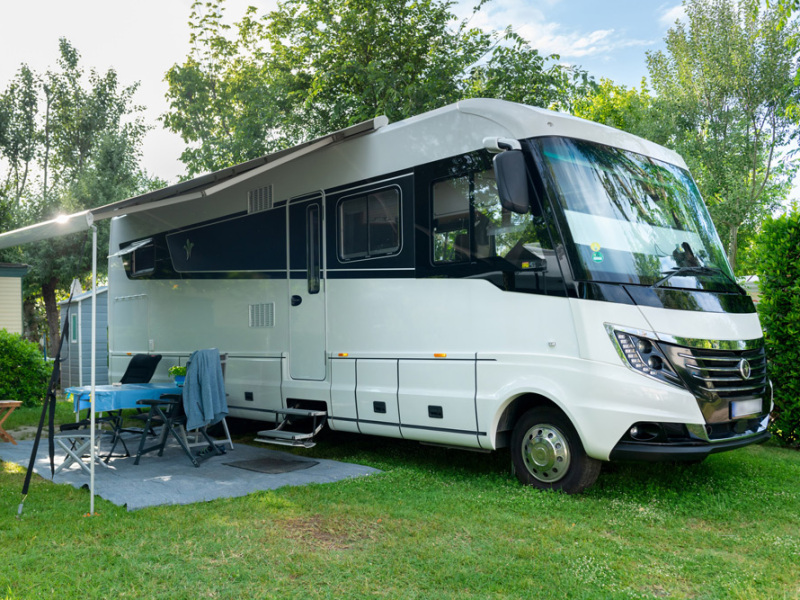 Camper parcheggiato con veranda aperta, tavolo e sedie su prato verde.