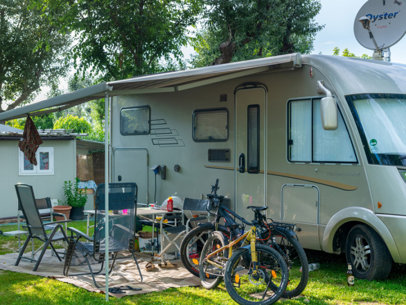 Camper con veranda, sedie, biciclette e piante in un'area verde.