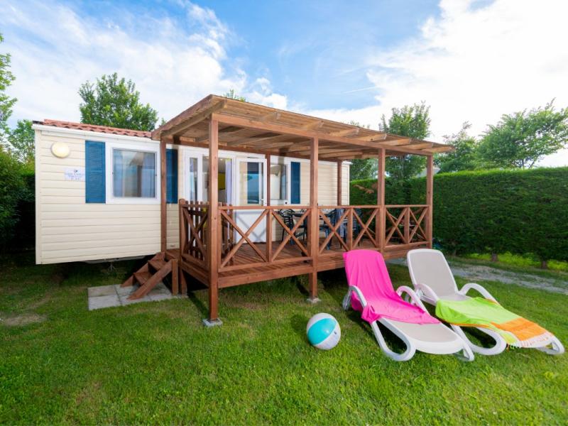 Casa mobile con veranda in legno, due lettini e pallone su prato verde.