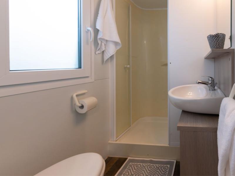 Bagno compatto con doccia, lavandino, finestra e accessori bianchi.