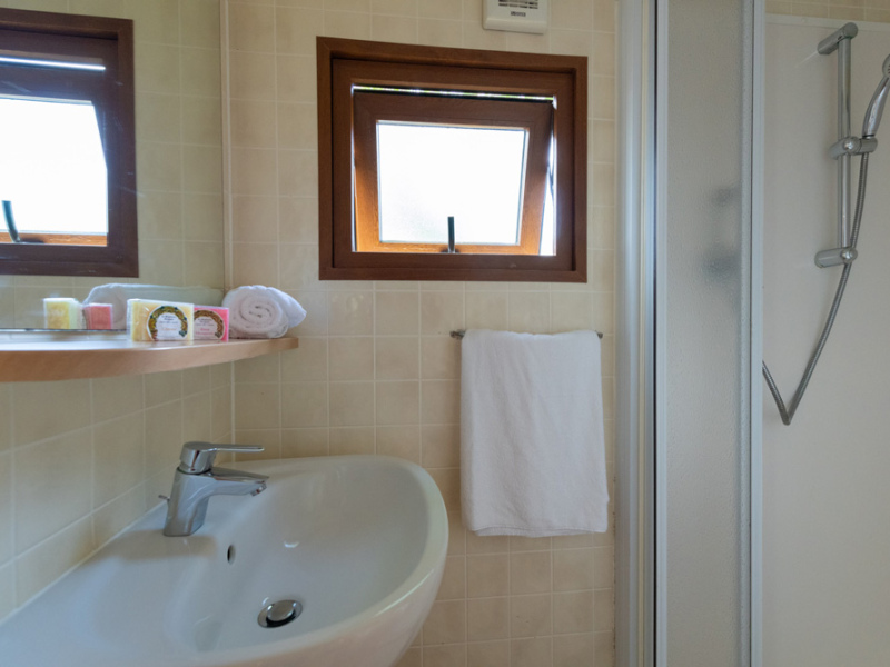 Bagno moderno con doccia, lavandino, finestre e asciugamani bianchi su mensola.