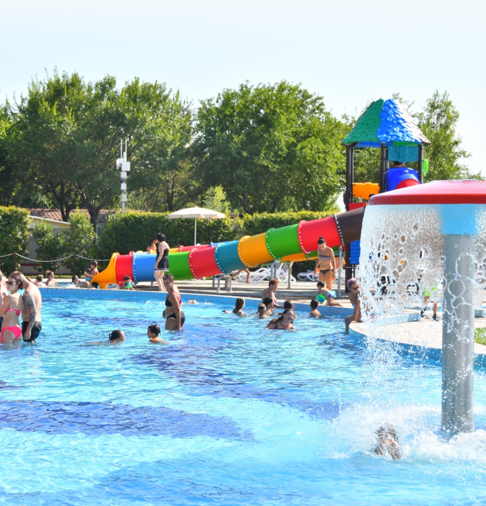 Piscina all'aperto con scivolo colorato e giochi d'acqua, persone che si divertono.