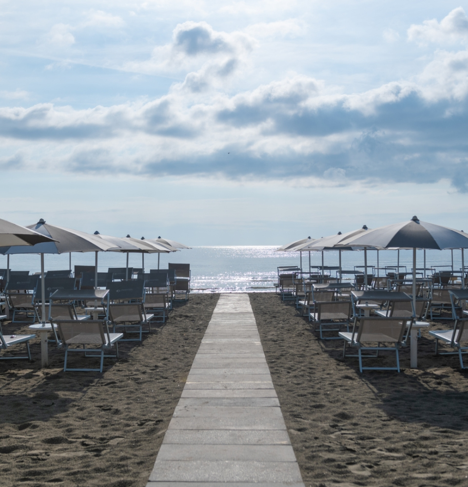 Spiaggia con ombrelloni e lettini, vista mare sotto un cielo nuvoloso.